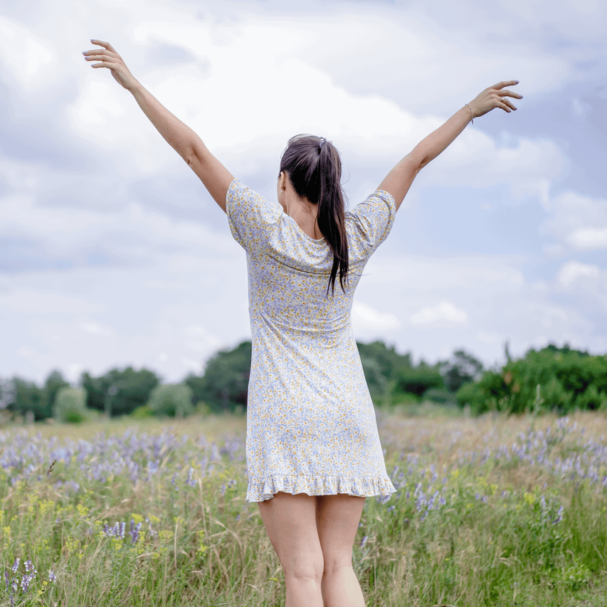 A woman enjoying freedom in a summer meadow, arms outstretched amidst blooming flowers. Captures a carefree moment of relaxation and joy.