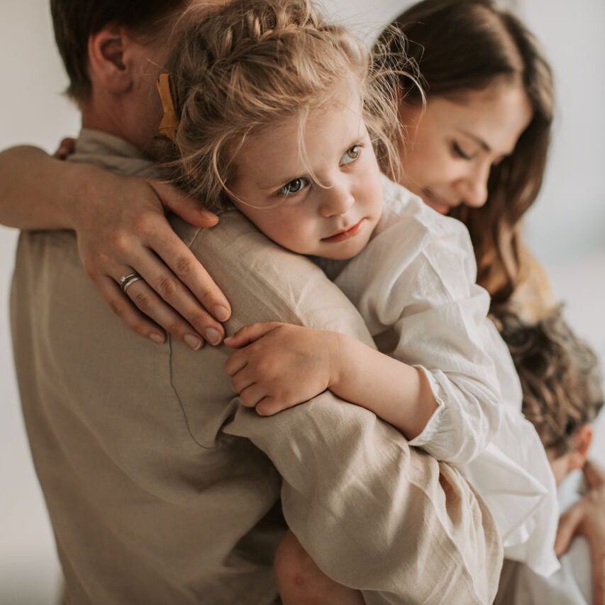 A young family shares a tender embrace inside a cozy home setting, highlighting love and togetherness.