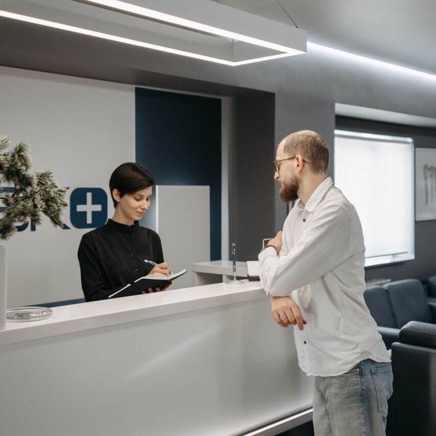 A man consults a receptionist in a modern clinic setting with contemporary design.